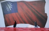 Des passants marchent devant le drapeau de Taïwan projeté lors d'un meeting du principal parti d'opposition, le Kuomintang, le 12 janvier à Nouveau Taipei