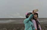 Des touristes prennent des selfies le 28 mars 2016 devant le volcan de boue qui a dévasté  Sidoarjo sur l'île de Java, en Indonésie