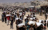 Des habitants de Gaza portent des sacs de farine qu'ils ont reçus après l'entrée de camions d'aide humanitaire par le point de passage de Zikim, dans le nord du territoire, le 27 juillet 2025