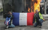 Des "gilets jaunes" brandissent un drapeau français sur lequel est écrit "liberté, égalité, fraternité, mon cul!" alors qu'un kiosque à journaux flamble sur les Champs-Elysées à Paris le 16 mars 2019