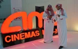 Des Saoudiens posent devant le logo du géant américain AMC Entertainment, première société autorisée à exploiter des cinélas eb Arabie saoudite, le 18 avril 2018 à Ryad