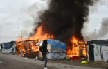 Un migrant court à côté d'un abri en flammes dans le bidonville géant de Calais (nord) en cours d'évacuation le 26 octobre 2016