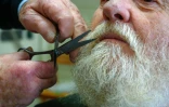 Le coiffeur Roger Amilhastre (G), âgé de 90 ans, taille la barbe d'un client dans son salon à Saint-Girons, en Ariège, le 16 avril 2024