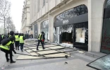 Des "gilets jaunes" devant la vitrine fracassée de la boutique Hugo Boss, pendant la manifestation des "gilets jaunes", sur les Champs-Elysées  à Paris, le 16 mars 2019