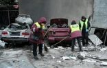Des employés municipaux dégagent des débris près de voitures détruites au pied d'un immeuble résidentiel endommagé après un bombardement russe à Kharkiv, le 26 février 2026 en Ukraine