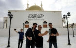 Des passants posent pour un selfie devant la mosquée Sahaba, dans la ville de Derna, dans l'est de la Libye, le 15 mai 2026, après des efforts de reconstruction et de réurbanisation entrepris plus de deux ans après les pluies extrêmes provoquées par la tempête Daniel