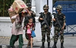 Une habitante, chargée de fruits et légumes, passe avec un enfant devant des soldats aux heures autorisées pendant un couvre-feu imposé pour rétablir la loi et l'ordre à Katmandou, le 12 septembre 2025 au Népal