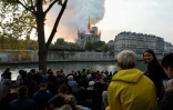Des passants regardent les flammes dévorer la toiture de la cathédrale Notre-Dame, le 15 avril 2019 à Paris