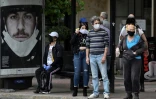 Des passagers, le visage couvert d'un masque de protection contre le coronavirus, attendent leur bus, au premier jour du déconfinement à Athènes le 4 mai 2020
