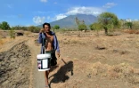 Un homme transporte des seaux sur un sentier à Bali le 26 septembre 2017 avec en toile de fond le mont Agung qui menace d'entrer en éruption, ce qui a provoqué l'évacuation de 75.000 habitants
