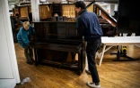 Des bénévoles déplacent un vieux piano dans l'atelier de "Pianodrome", le 9 février 2023 à Edimbourg, en Ecosse