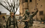 Des combattants des Forces démocratiques syriennes (FDS) prennent un "selfie" avec un téléphone dans le village de Baghouz (est de la Syrie), repris la veille aux jihadistes du groupe Etat islamique (EI) dont le "califat" a été éradiqué, le 24 mars 2019