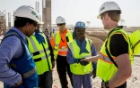 Un technicien salue un ouvrier portant une veste réfrigérante, lors de la construction du stade de Losail, le 30 août 2018 à Doha, qui accueillera les matches d'ouverture et de clôture du Mondial 2022 travaillent sur le chantier du stade de Lusail (Qatar), une enceinte de 80.000 places, le 15 décembre 2018, qui accueillera les matches d'ouverture et de clôture de la Coupe du monde de football 2022