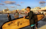 Le Palestinien Tahseen Abu Assi porte sa planche de surf sur une plage de la ville de Gaza, le 21 juin 2026