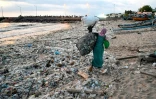 Une femme porte des sacs de déchets recyclables récupérés dans les ordures échouées sur la plage de Kedonganan, sur l'île indonésienne de Bali, le 19 mars 2024