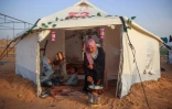 Une Palestinienne prépare à manger à côté d'enfants assis dans une tente de déplacés, avant le repas de rupture du jeûne pendant le mois  musulman du ramadan, dans le camp de Bureij, dans le centre de la bande de Gaza, le 5 mars 2025