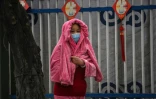 Une femme se couvre de la pluie devant le centre communautaire de Jiangxinyuan où les membres de l'équipe de l'Organisation mondiale de la santé (OMS) qui enquête sur les origines du coronavirus COVID-19 se rendent à Wuhan, dans la province centrale du Hubei, en Chine, le 4 février 2021.