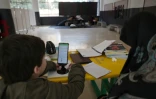 Une femme, assise à côté d'un enfant, supervise ses études en ligne sur un téléphone portable dans une école publique transformée en refuge pour personnes déplacées, à Dekwaneh, au nord de Beyrouth, le 25 mars 2026 au Liban
