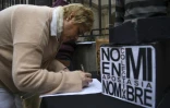 Une femme paraphe un document renonçant à son baptême à côté d'une pancarte disant "Pas en mon nom. Apostasie collective", devant le siège de la conférence épiscopale argentine, le 24 août 2018