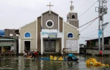 Des ouvriers déchargent des sacs de sable sur un chantier de construction devant une église dans une rue inondée de l'île de Pugad, dans la province de Bulacan, le 21 août 2025 aux Philippines