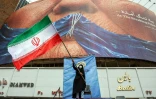 Une femme agite un drapeau iranien devant un panneau anti-américain en référence à Donald Trump et à la fermeture du détroit d'Ormuz, le 5 mai 2026 à Téhéran