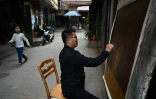 L'artiste Wu Feimin peint un tableau dans une allée du village de Dafen, le 19 février 2023 en Chine