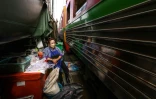 Une vendeuse de poisson du marché de Maeklong assise à son étal au passage d'un train de passagers, dans la province de Samut Songkhram, le 4 juin 2022 en Thaïlande