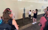 Des passants prennent des photos pendant que la peintre en décor du patrimoine, Agnès Perrone, répare une œuvre d'art de l'artiste de rue Banksy représentant un phare sur la façade d'un bâtiment, après qu'elle a été vandalisée pendant la nuit à Marseille, le 1er juin 2025