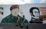 Des miliciens passent devant une fresque murale figurant l'ancien président vénézuélien Hugo Chavez et le libérateur Simon Bolivar, le 7 janvier 2025 à Caracas