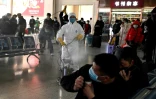 Des passagers se protègent alors qu'un homme désinfecte le hall de la gare de la ville de Hefei (province de l'Anhui), le 4 mars 2020