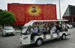 Des touristes à bord d'une voiturette électrique passent devant une fresque de Mao Zedong, place de "L'Orient est route", à Nanjie, dans la province du Henan, le 20 août 2026 en Chine