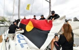 L'équipage du "Tribal Warrior" (Guerrier Tribal) hisse le drapeau aborigène dans le port de Sydney en Australie, le 13 décembre 2019, lors d'un exercice avant le départ de la course Sydney-Hobart ce jeudi.