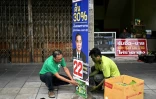 Phongsa Choonaem (g), dirigeant et fondateur du parti vert, colle une affiche sous un poster du Premier ministre Prayut Chan-O-Cha, lors de la campagne électorale, le 30 avril 2023 à Bangkok, en Thaïlande
