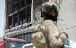 Un membre des forces de sécurité irakiennes devant la façade incendiée du centre commercial Hyper Mall de Kut, dans l'est de l'Irak, le 17 juillet 2025