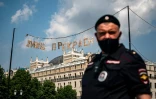 Un policier russe masqué pose sous une banderolle qui proclame "la vie est belle", dans le centre de Moscou, le 9 juin 2020. 
