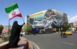 Une femme tient le drapeau iranien près d'une affichage géante "Le détroit d'Ormuz reste fermé", le 5 avril 2026 à Téhéran