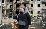 Une femme avec un enfant marche devant un immeuble résidentiel endommagé dans la rue Koshytsa, une banlieue de la de  Kiev, le 25 février 2022.