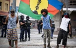 Des habitants indépendantistes jouent à la pétanque, tout en déployant un drapeau du FLNKS, sous le regard des forces de sécurité à Nouméa, dans le quartier de la valllée du Tir, le 24 septembre 2024