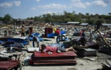 Un homme s'est allongé sur des tôles empilées au milieu des décombres, le 1er octobre 2018 à Palu dans l'île des Célèbes en Indonésie, tandis que d'autres cherchent à récupérer des objets quatre jours après un séisme meurtrier