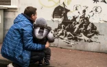 Un homme et un enfant regardent un pastiche de la célèbre toile "Le radeau de la méduse" peint par Bansky sur un mur non loin de la mairie de Calais, le 12 décembre 2015