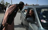 Un combattant taliban travaillant comme policier contrôle les passagers d'une voiture à Kaboul le 3 octobre 2021 