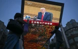 Des personnes passent devant un écran sur lequel est visible Donald Trump, le 14 mai 2026 à Pékin