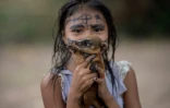 Une jeune Arara tient un bébé raton laveur au camp tribal Laranjal, en Amazonie brésilienne, le 15 mars 2019