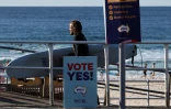 Un surfeur passe à côté d'affiches appelant à voter "oui" au référendum sur les droits des Aborigènes, le 14 octobre 2023 à Sydney, en Australie
