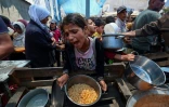 Une fillette reçoit de la nourriture tandis que d'autres Palestiniens attendent à un point de distribution de repas à Nousseirat, dans le centre de la bande de Gaza, le 2 juin 2025