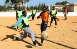 Des migrants Camerounais (orange) et Sénégalais (jaune) participent à un match de football au camp de Tarjoura en Libye, le 28 février 2018