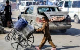 Une fillette palestinienne pousse un fauteuil roulant cassé chargé de jerrycans le long d'une route dans un camp de déplacés à Nousseirat, dans le centre de la bande de Gaza, le 7 octobre 2025
