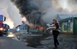 Une femme près d'un épais panache de fumée s'élevant depuis un marché aux livres après une attaque aérienne russe, le 16 août 2026 à Kiev 