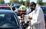 Un prêtre portant un masque de protection dépose une hostie dans la main d'un automobiliste garé sur un parking pour assister à une messe en plein air célébrée par Mgr François Touvet, l'évêque de Châlons-en-Champagne, le 17 mai 2020