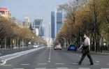 Un homme portant un masque et des gants traverse l'avenue La Castellana généralement très fréquentée, le 15 mars 2020 à Madrid
